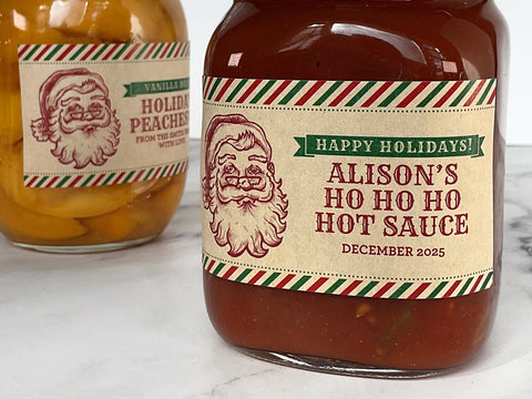 Two mason jars filled with food. One jar has red hot sauce and the other has spiced peaches. Both jars are decorated with Custom Kraft Santa Christmas Rectangle Canning Labels. The labels have a nostalgic drawing of Saint Nick with custom printed text with a red & green peppermint striped border | CanningCrafts.com
