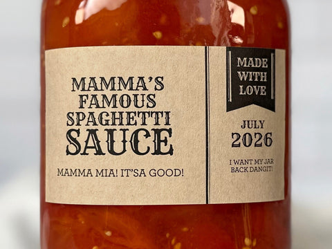 A mason jar filled with red spaghetti sauce with a rectangular kraft paper canning label wrapped around it. The Apothecary Style Canning Label has black text with a cute pennant banner with text reading Made With Love. Each label is custom printed with text for the food inside such as Spaghetti Sauce. | CanningCrafts.com
