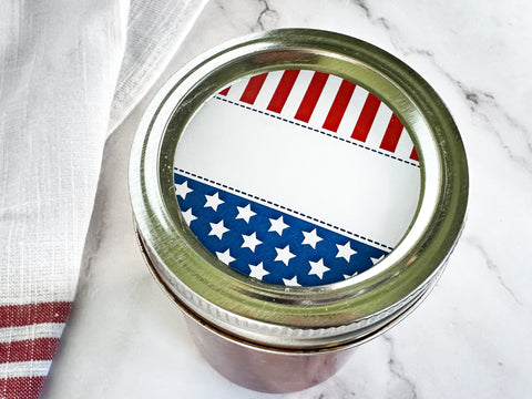Blank Star Spangled Canning Labels on top of a mason jar lid. The patriotic canning jar label artwork shows red, white, and blue American flag graphics with room to handwrite text for the jar contents | CanningCrafts.com